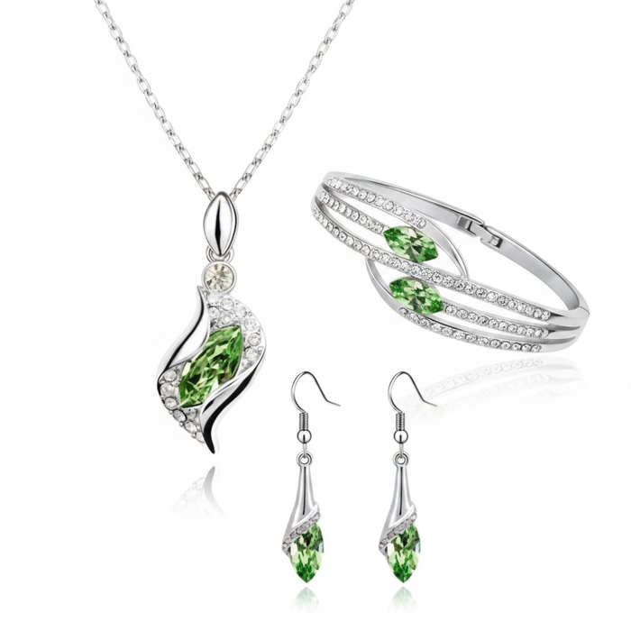 An elegant silver jewelry ensemble featuring a marquise-cut green crystal pendant necklace, matching drop earrings, and a multi-strand crystal-encrusted bangle on a reflective white background.