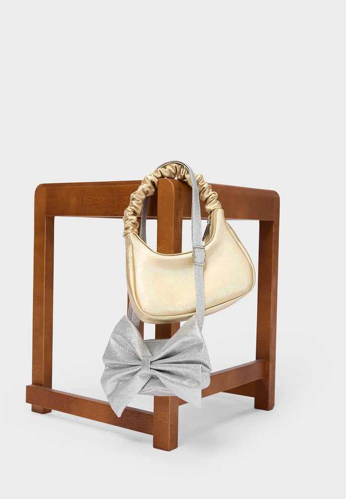 Gold handbag and gray bow on a wooden stand against a white background