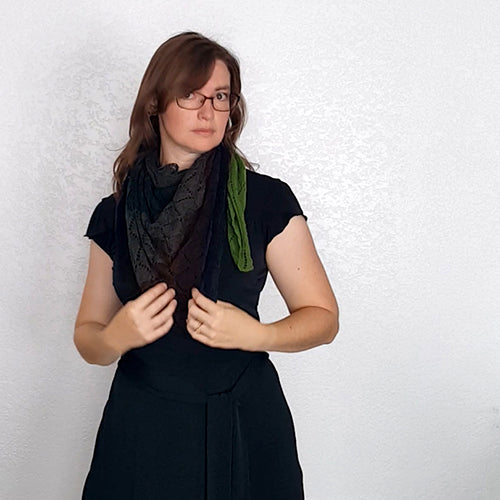 Model wearing two Kellerwald shawls layered together — one in charcoal black and one in green — wrapped around her neck and shoulders over a black dress
