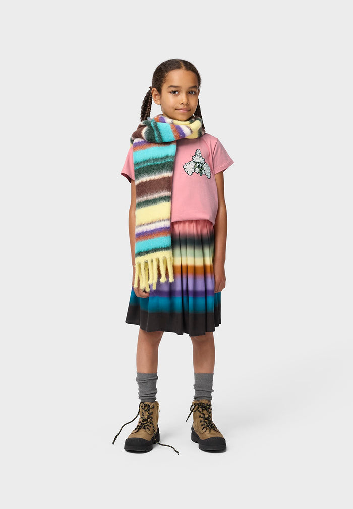 Young girl wearing a colorful scarf, pink shirt, black skirt, and brown boots on a white background