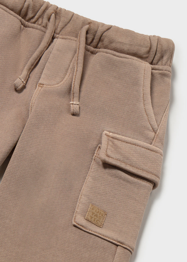 Close-up of beige cargo pants with a brand label on a light gray background