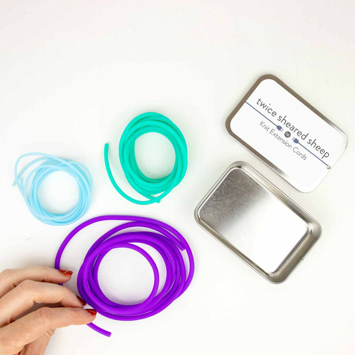 Knit Extension Cords stitch holder set showing teal and purple silicone cord rings in multiple sizes with a Twice Sheared Sheep storage tin on white background
