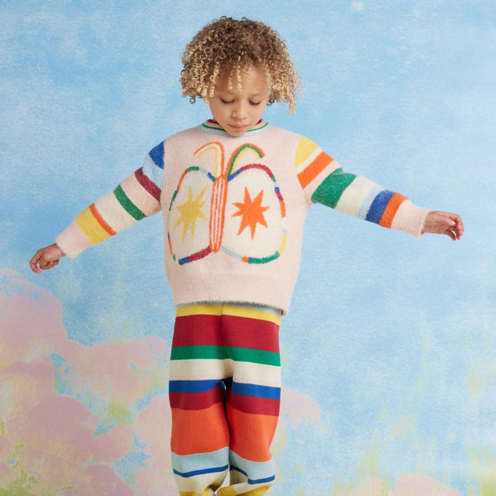 Child wearing a colorful sweater and striped pants against a pastel background