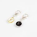 Two lobster claw clip stitch markers with gold-framed P for purl on white and silver-framed K for knit on black enamel charms