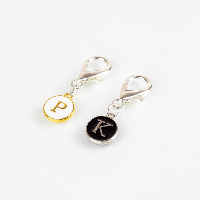Two lobster claw clip stitch markers with gold-framed P for purl on white and silver-framed K for knit on black enamel charms