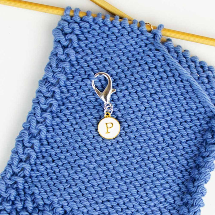 Close-up of P reminder clip marker attached to garter stitch side of blue knitting on bamboo needle