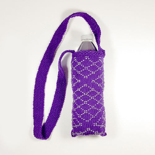 Purple knitted water bottle holder with silver beaded diamond lattice pattern and long garter stitch shoulder strap, shown with a water bottle inside