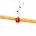 Close-up of red and black enamel ladybug charm on numbered bead chain row counter resting on bamboo knitting needle