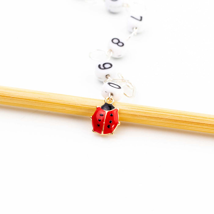 Close-up of red and black enamel ladybug charm on numbered bead chain row counter resting on bamboo knitting needle