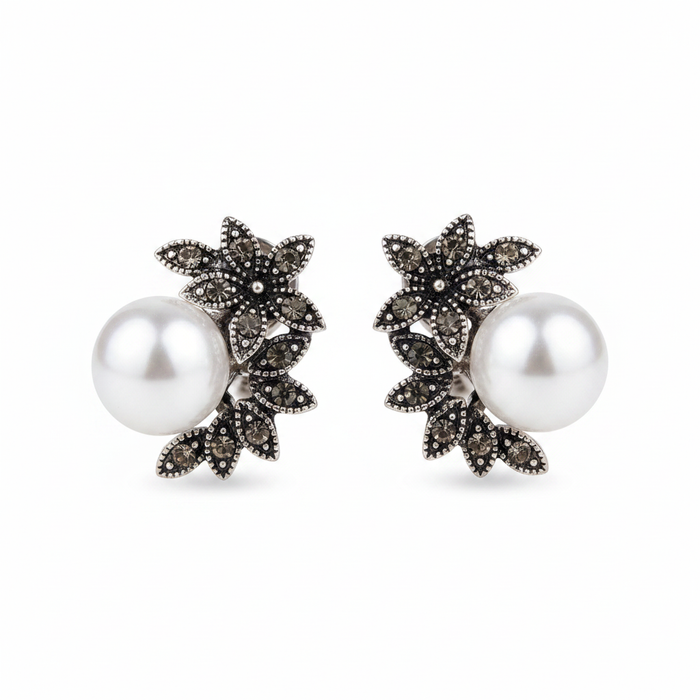 Pair of antique silver-tone stud earrings featuring an intricate floral leaf design set with dark grey marcassite stones and a large, high-luster white pearl, displayed on a clean white background.