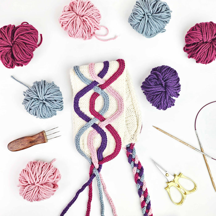 Close-up of freeform i-cord cables in pink and cream yarn being created with the Cord Quill tool, showing the textured cable shapes on knit fabric