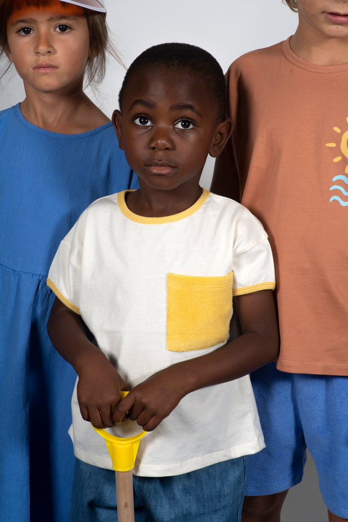 Three children standing together, with a focus on a child in the center wearing a white shirt with yellow accents.
