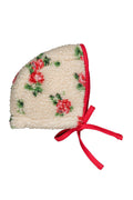 A cream-colored fleece bonnet featuring a red and green floral pattern and a red ribbon tie, shown on a plain white background.
