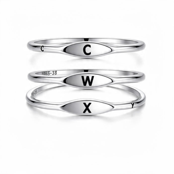 Three polished silver rings stacked vertically on a white background, each with an oval face engraved with a black capital letter: C on the top ring, W on the middle ring, and X on the bottom ring.