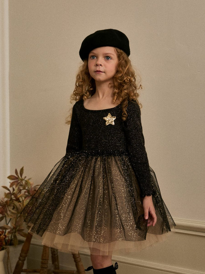 Young girl wearing a tutu dress against a beige wall.