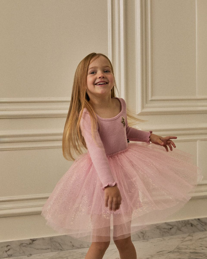 Young girl in a pink dress standing in a room with decorative walls.