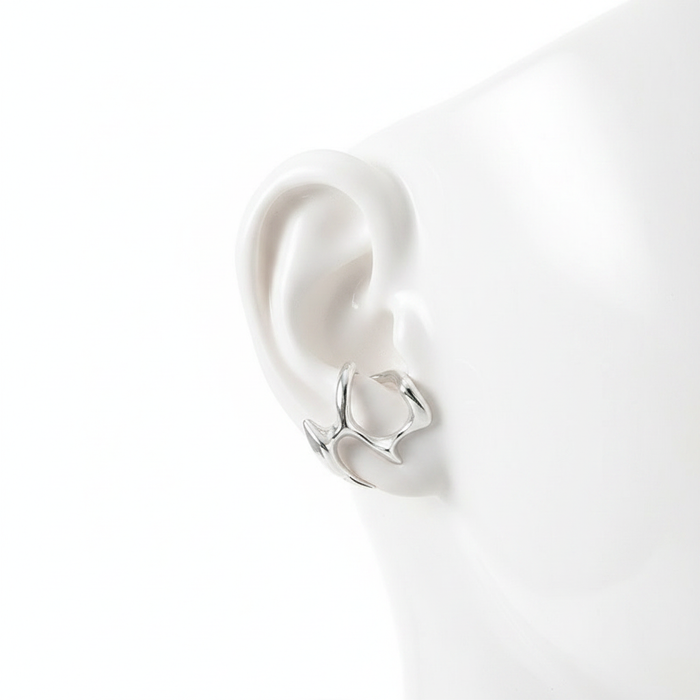A minimalist silver-toned ear cuff with an organic molten metal design, displayed on a white mannequin ear to show its unique wrap-around fit.