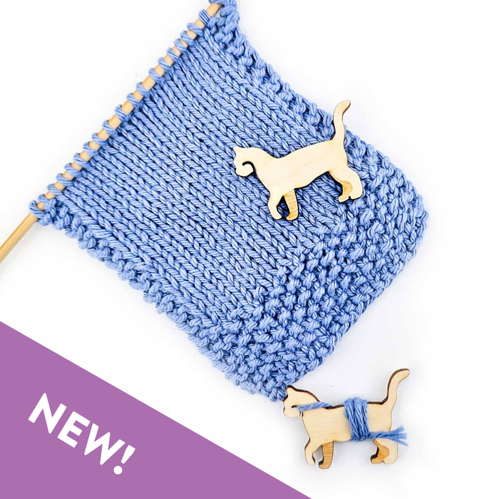 Single wooden cat-shaped yarn bobbin in natural birch laser-cut silhouette on blue garter stitch knit fabric with NEW banner