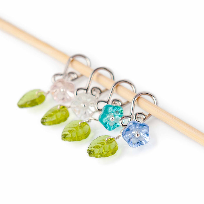 Little Flowers melody clip stitch markers with glass flower beads in pink, clear, teal, and blue with green leaf charms on bamboo needle