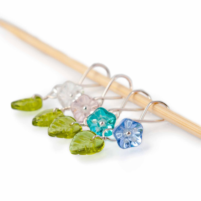 Little Flowers infinity ring stitch markers with glass flower beads in pink, clear, teal, and blue with green leaf charms on bamboo needle