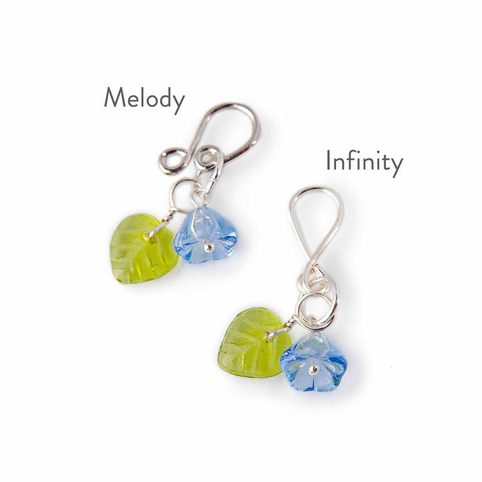 Close-up comparison of Melody and Infinity style Little Flowers stitch markers with blue glass flower and green leaf bead
