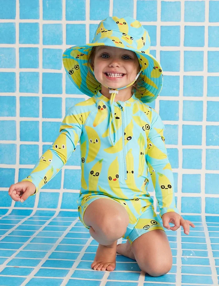 Child wearing a yellow and blue swimsuit with a matching hat on a blue tiled background