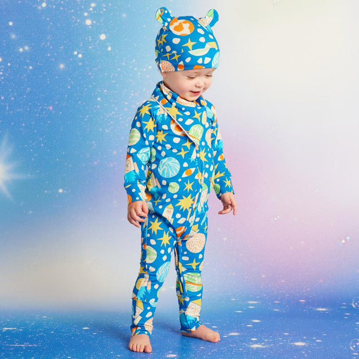 Child wearing a blue patterned onesie and hat against a starry sky background