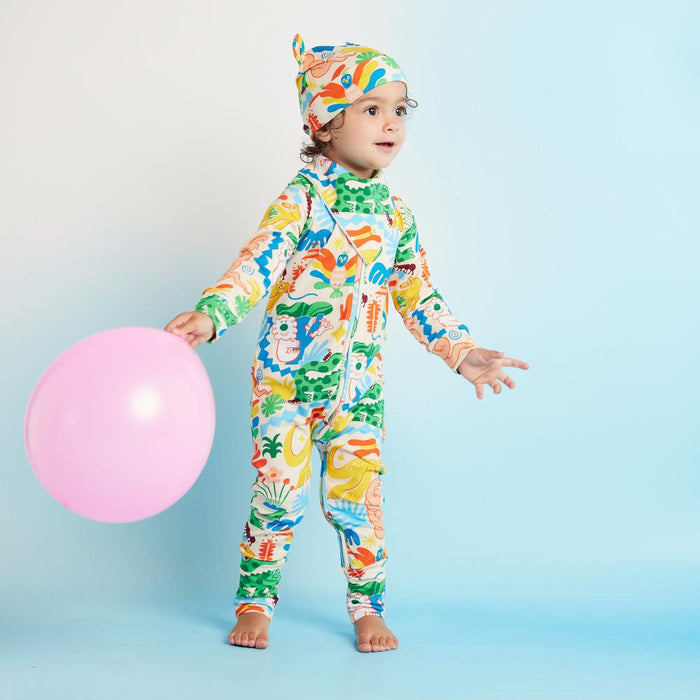 Child wearing a colorful onesie and headband, holding a pink balloon on a light blue background.