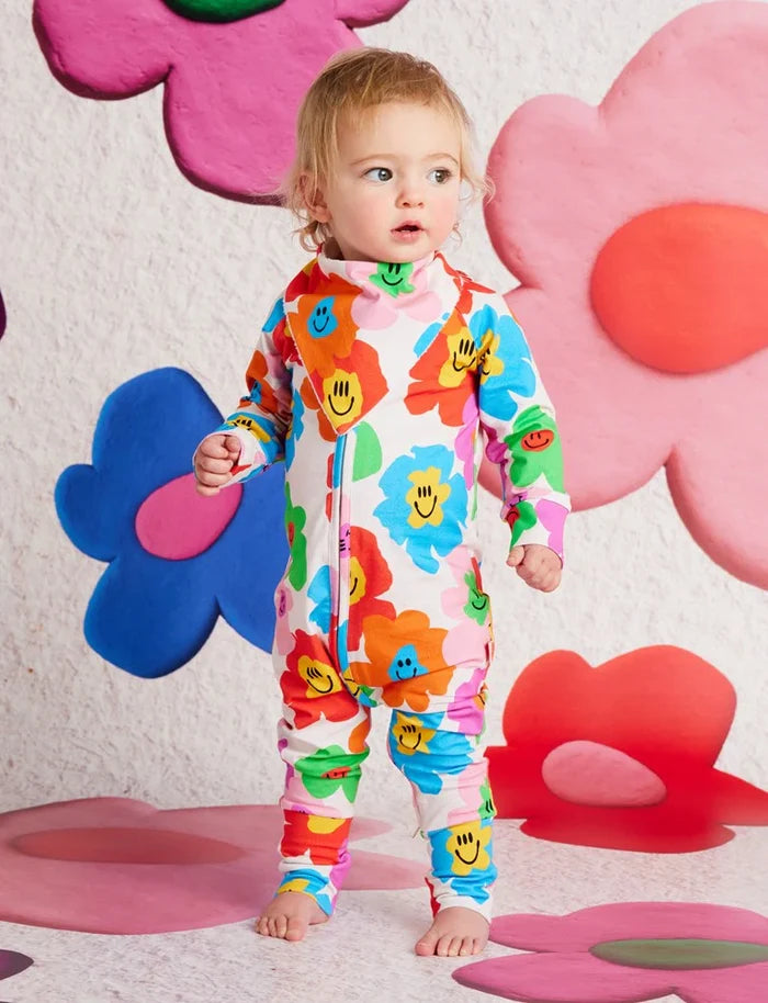 Child wearing a colorful floral onesie with a playful background of oversized flowers.
