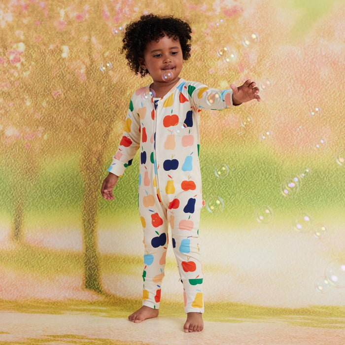 Child wearing a colorful onesie with a pattern of various shapes, standing in a garden with blurred background.