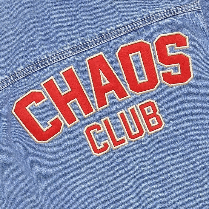 Close-up of a light blue denim jacket featuring red collegiate-style embroidered text reading 'CHAOS CLUB' with a cream outline.