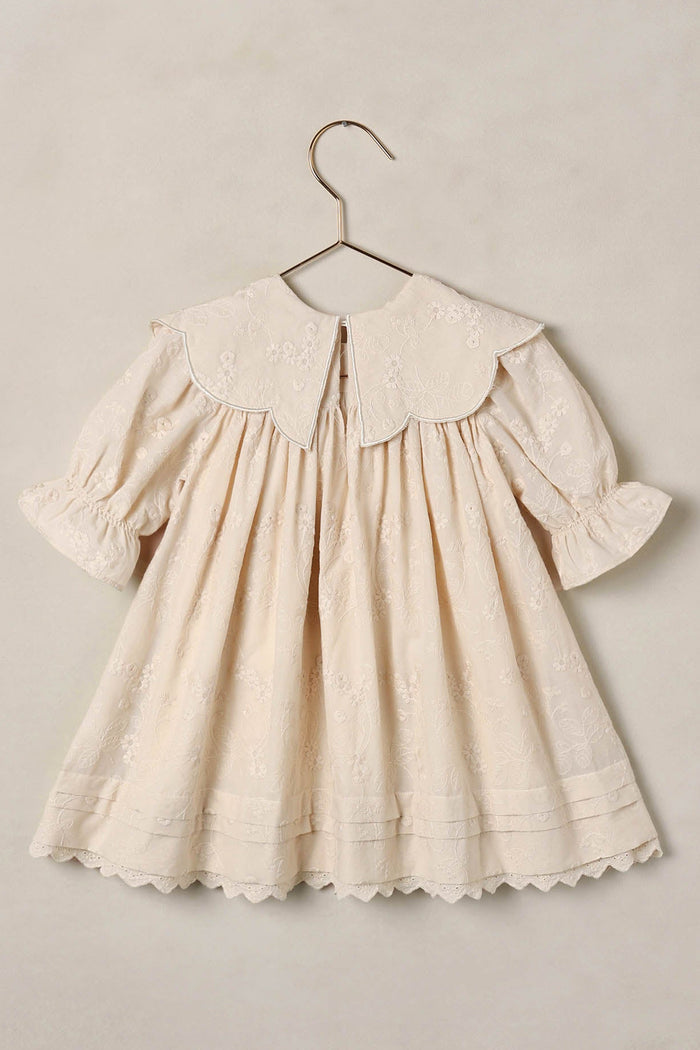 Cream-colored dress with a collar on a hanger against a beige background