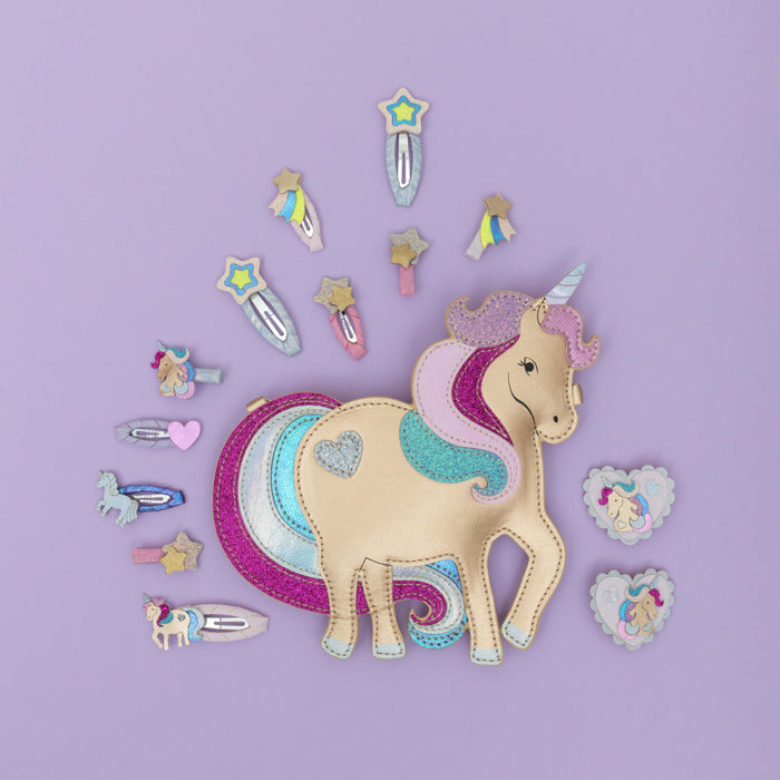A unicorn-themed hair accessory set arranged on a lavender background, featuring a central unicorn purse  with a glittery multicolor mane and tail, surrounded by matching hair clips and small heart-shaped charms.