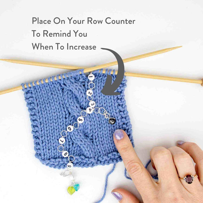 Instructional image showing reminder clip marker placed on row counter chain to mark increase rows in knitting