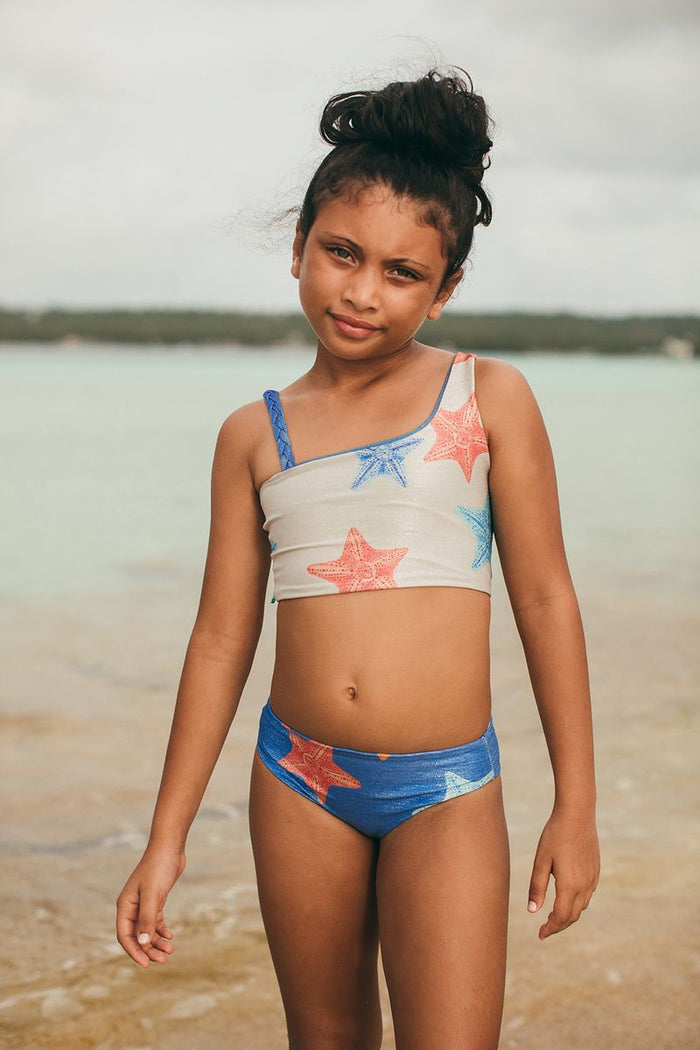 Young girl in a colorful swimsuit standing on a beach