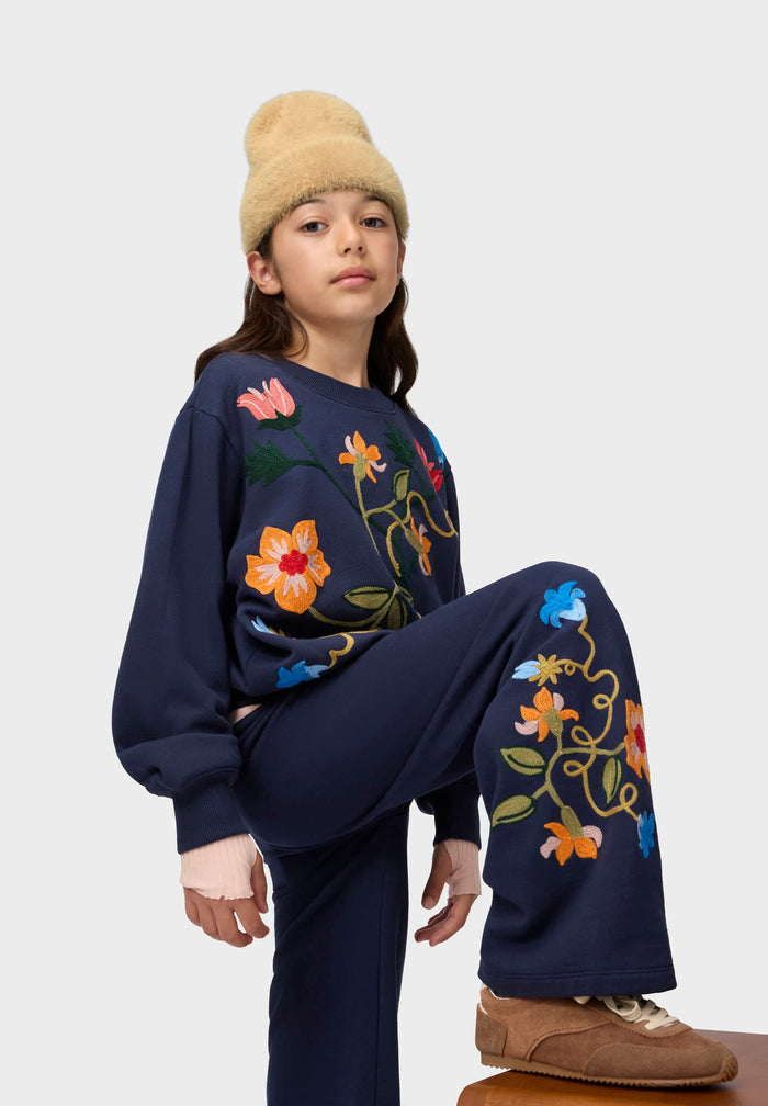 Person wearing a navy blue outfit with colorful floral embroidery on a white background
