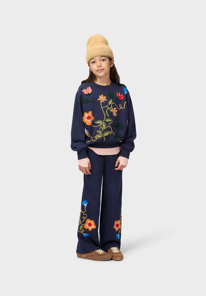 Person wearing a navy sweater with floral embroidery on a white background