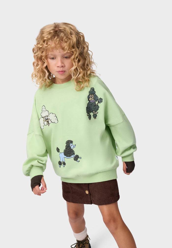 Child wearing a light green sweater with poodle designs on a white background