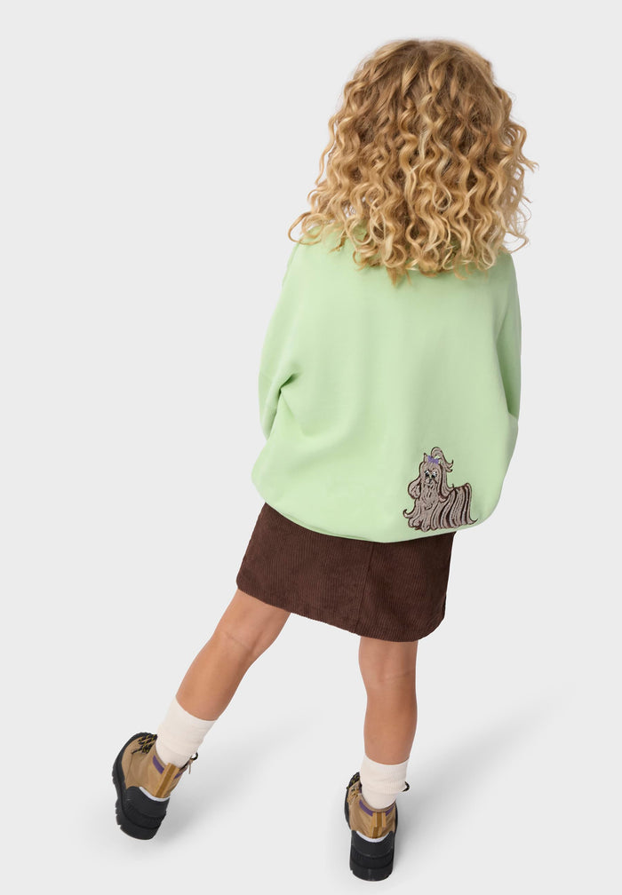 Child wearing a light green sweater with a design and a brown skirt on a white background