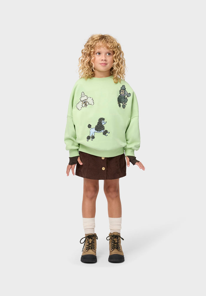 Child wearing a light green sweater with poodle designs on a white background