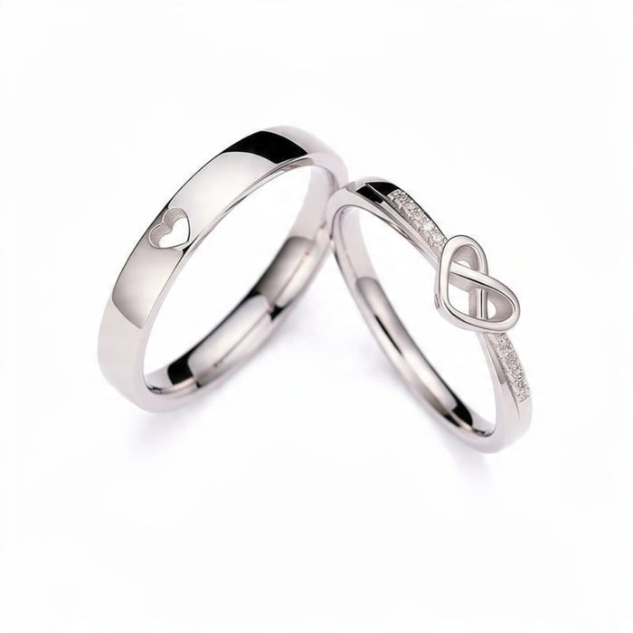 Two adjustable platinum tone couple rings on white background, one band with heart cutout design and one with infinity symbol and crystal stones, matching his and hers promise rings set