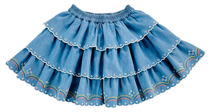 A tiered blue denim skirt with white embroidered details and rainbow patterns near the hem, shown against a plain white background.