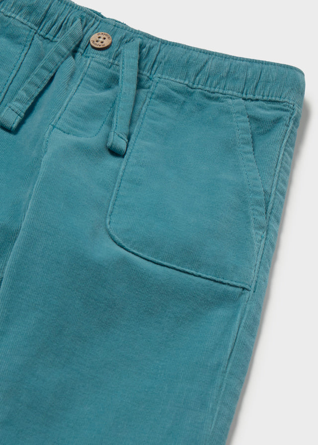 Teal pants with a button and strap on a light gray background
