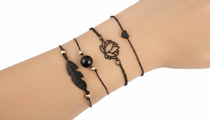 Stacked set of 4 matte black bracelets featuring a lotus flower, feather charm, and heart detail on a wrist