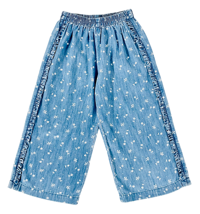 Light blue denim cropped pants with a white floral print and ruffled trim along the sides, shown flat on a white background.