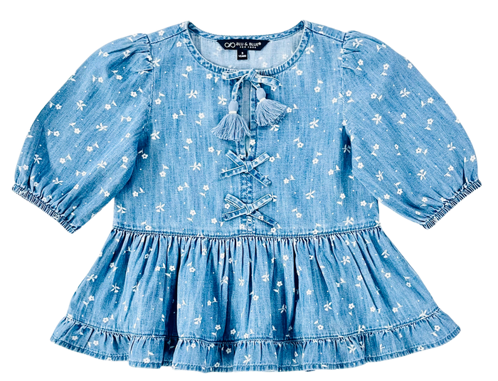 A light blue denim-like top with a white floral print, featuring puff sleeves, a tassel tie neckline, and lace-up front detailing.