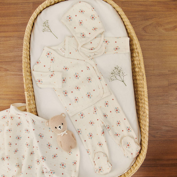 Baby outfit with floral pattern in a wicker crib on a wooden floor