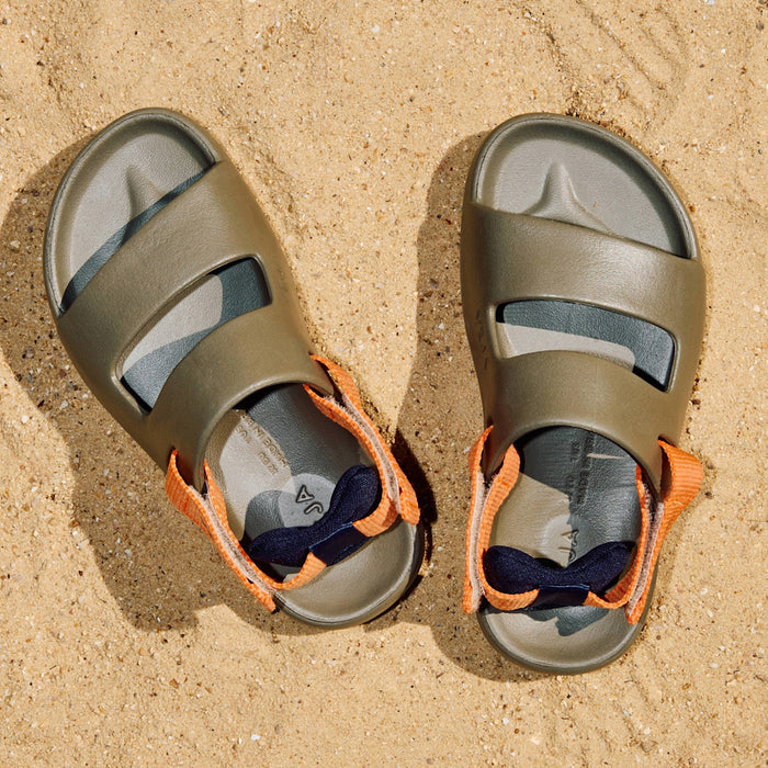 Pair of green sandals with orange straps on a sandy surface