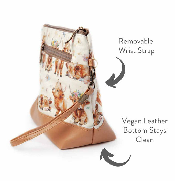 Maisy the Highland Cow Mini Trini Bag side view showing the removable wrist strap, zippered exterior back pocket, and vegan leather bottom with annotated feature text