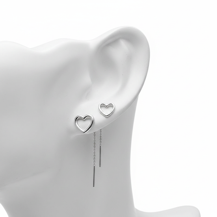 A high-resolution, close-up shot of silver open-heart stud earrings and long threader earrings with sleek bar drops, displayed on a white mannequin ear against a pure white background.